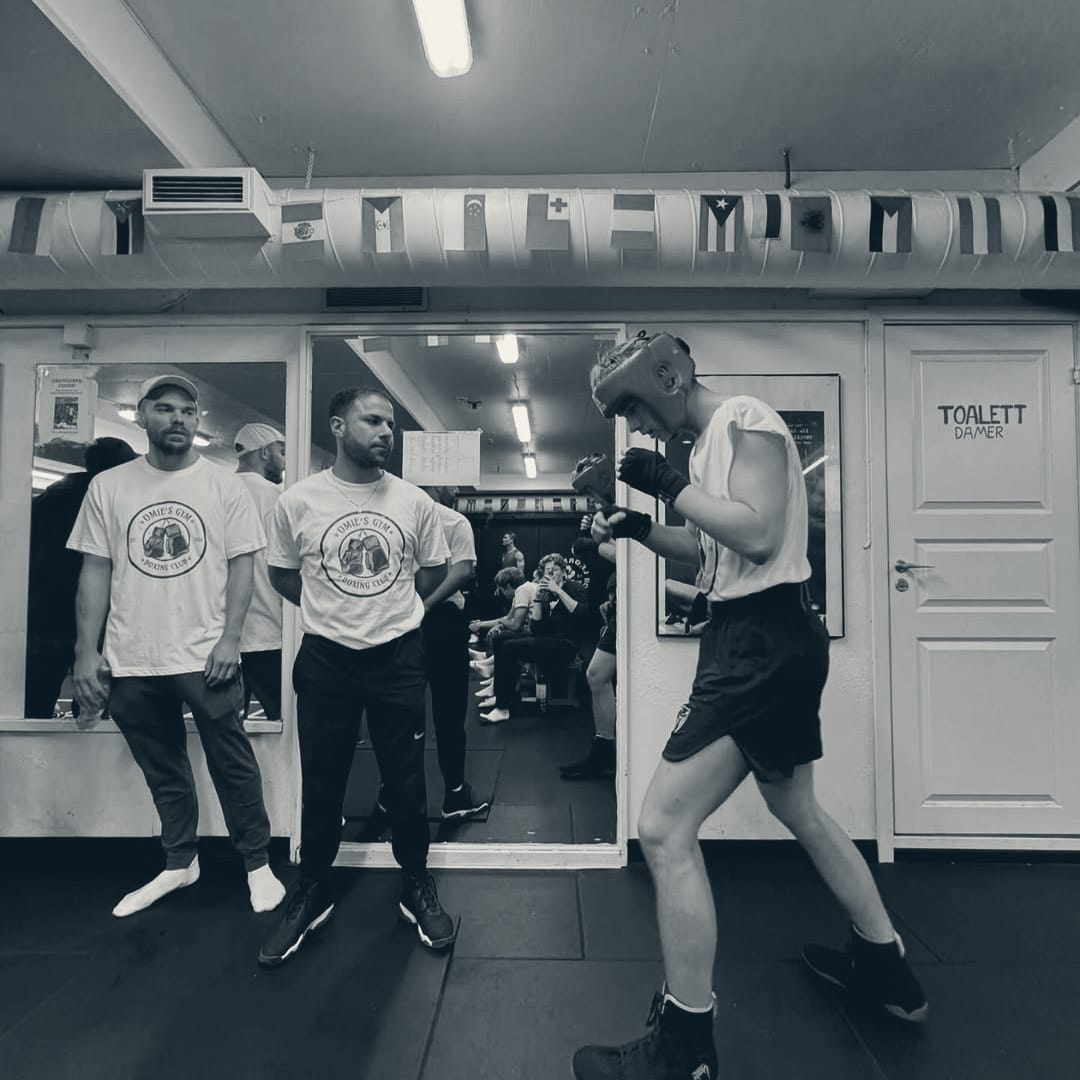 To trenere i Omie's Gym-t-skjorter og en bokser i rød hodebeskytter før en kamp på stevne
