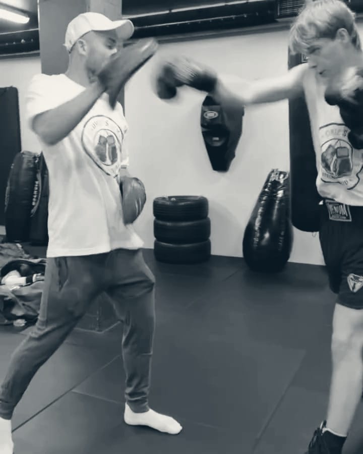 Trener i Omie's Gym-t-skjorte holder puter mens en ung bokser slår, på en privattime i boksing